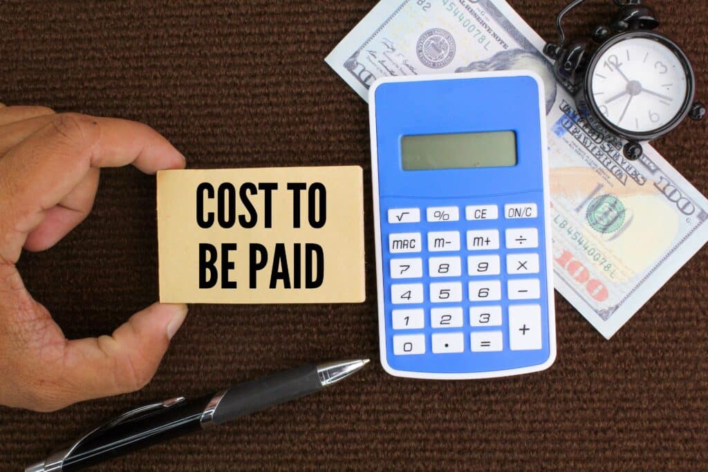 Taschenrechner, Stift und Papiergeld mit dem Wort „zu zahlende Kosten“.